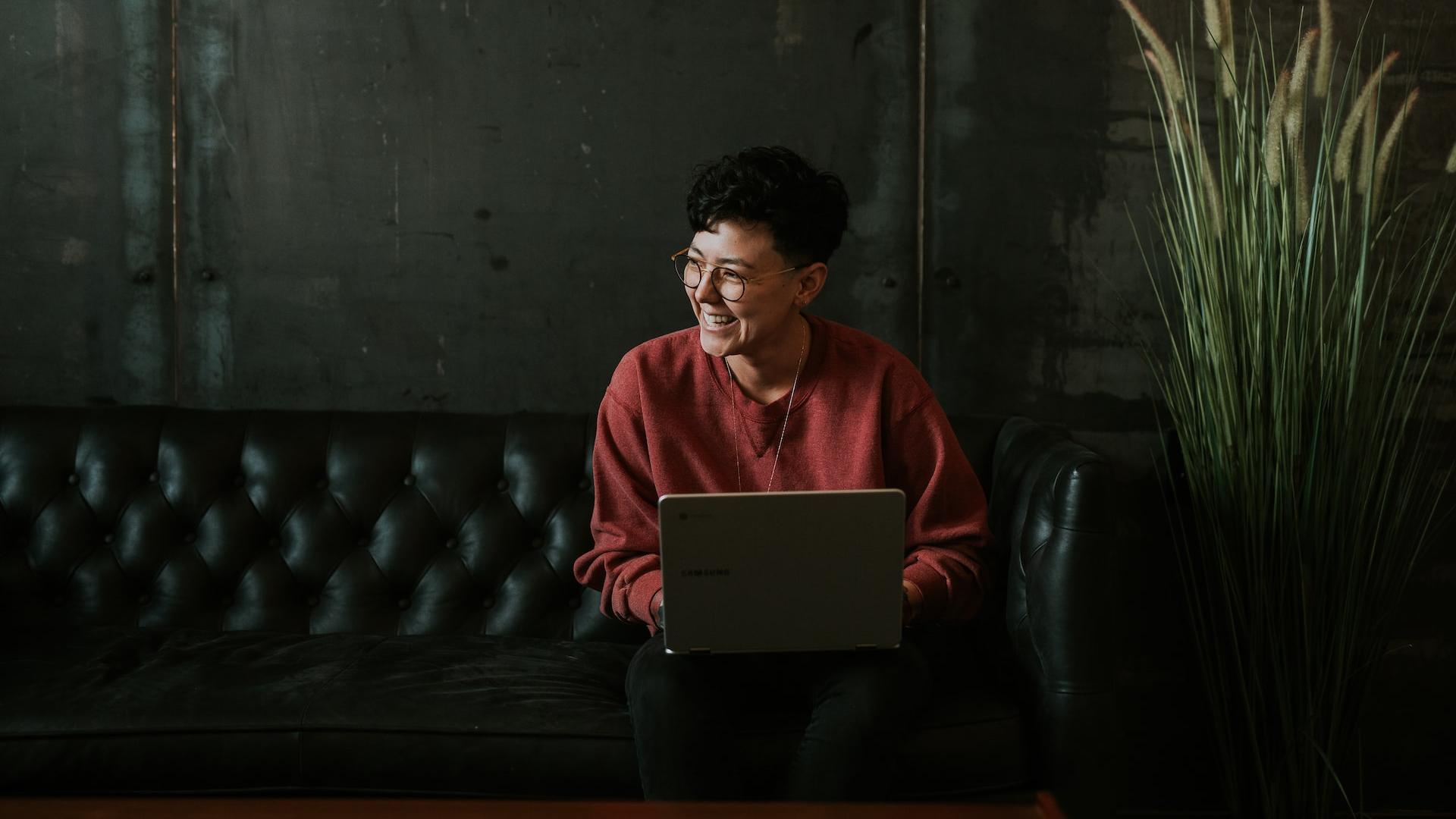 smiling man using laptop computer while sitting on black leather sofa